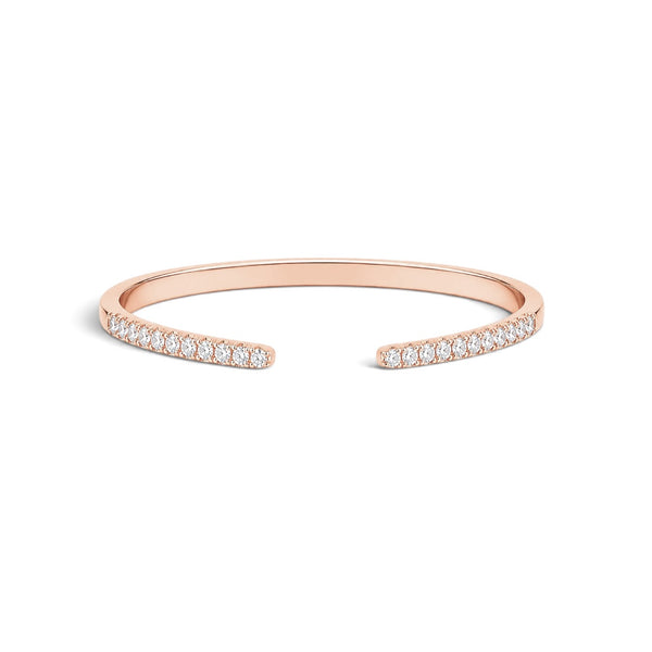 A slim open cuff bracelet in rose gold, featuring rows of small clear stones along both ends, shown on a plain white background.