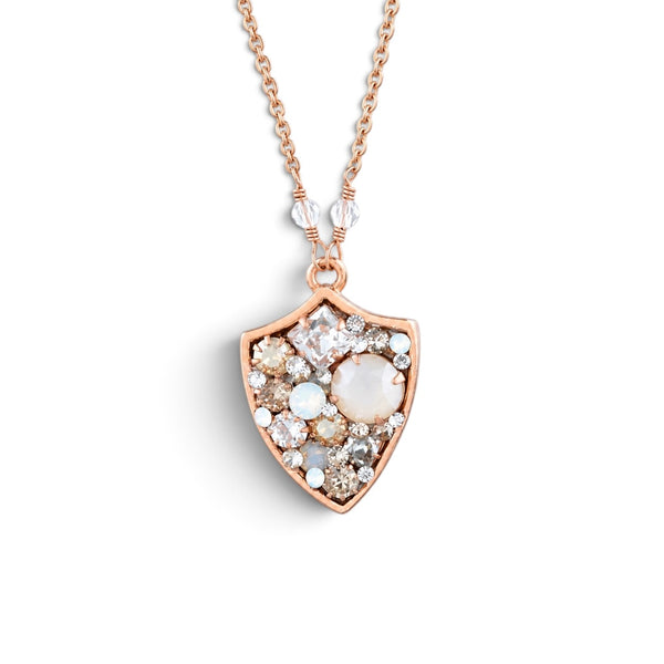 A rose gold shield pendant necklace featuring a central milky white oval stone surrounded by small clear and champagne-colored stones, suspended from a delicate rose gold chain on a white background.